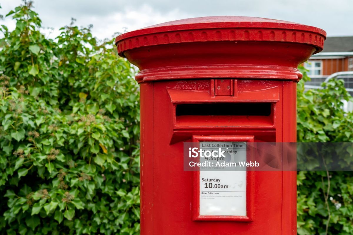 A red pillar box beside a hedge on a British street